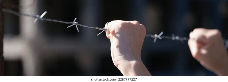 Close-up of woman hands holding metal security barbedwire fence. Wire with clusters of short, sharp spikes. Fence or warfare obstruction, correctional institution concept