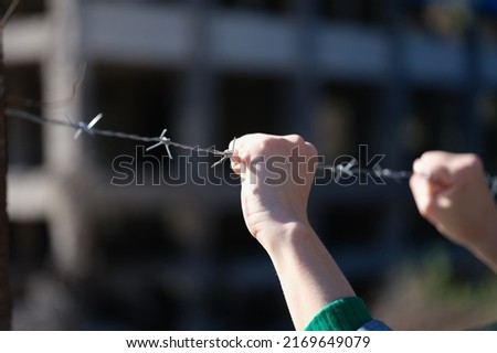 Close-up of woman hands holding metal security barbedwire fence. Wire with clusters of short, sharp spikes. Fence or warfare obstruction, correctional institution concept