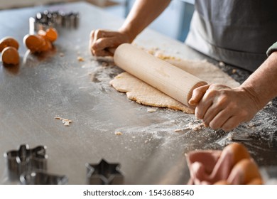 Closeup Of Woman Hands Holding Rolling Pin To Flatten Dough On Kitchen Counter. Old Woman Rolling Dough For Cookie On Platform At Home With Ingredient Around. Mature Woman Cooking Christmas Cookies.