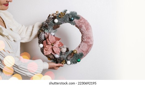 Close-up woman holding beautiful Christmas wreath. The basis of the wreath is spruce branches, no waste festive decor in female hands. Banner - Shutterstock ID 2230692195