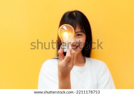 Close-up of a woman holding a glowing light bulb creative business ideas Inspired idea with light bulbs on yellow background. Ideas for success. hand holding incandescent lamp