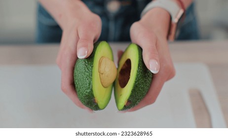 Close-up of a woman holding half of fresh ripe avocado in hand, top view. - Powered by Shutterstock