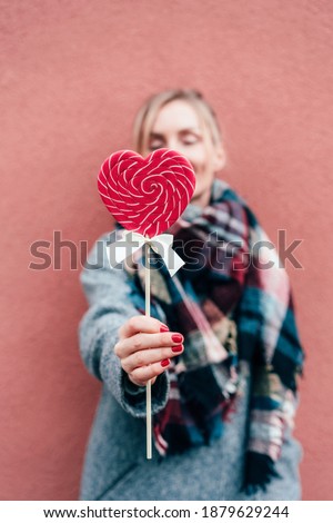 Close-up of a woman holding a heart shaped caramel lollipop. Valentine's day content and date. Romantic mood. Be my Valentine.