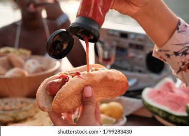 Close-up of woman holding hot dog and adding ketchup on it during dinner - Powered by Shutterstock