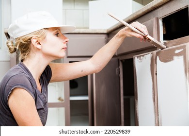 Closeup Of Woman Holding Paint Brush And Painting Kitchen Cabinets