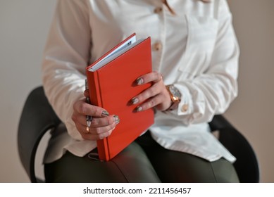 Closeup Of A Woman Holding A Red Notebook, Taking Notes.Girl Holding A Red Notebook For Writing. Large Portrait Of A Notebook.