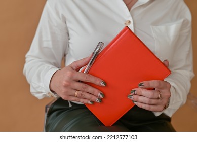 Closeup Of A Woman Holding A Red Notebook, Taking Notes.Girl Holding A Red Notebook For Writing. Large Portrait Of A Notebook.