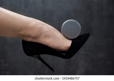 Closeup woman leg in black high heel shoes with balm or cream in round metal jar, on grey background