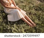 Close-up of a woman in a light summer dress sitting in a sunlit meadow, enjoying the warmth and tranquility. Perfect for concepts of relaxation, nature, and summer, ideal for lifestyle and travel