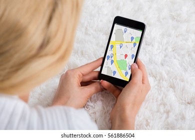 Close-up Of A Woman Lying On Carpet Using GPS Navigation Map On Mobile Phone