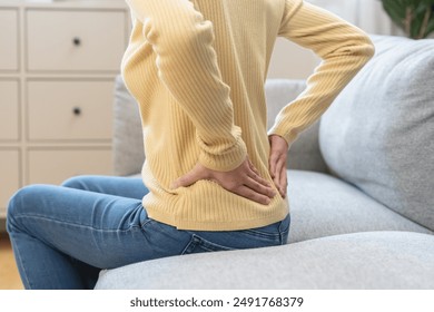 Close-up woman massaging her lower back has back pain because of sitting posture during work in office. - Powered by Shutterstock