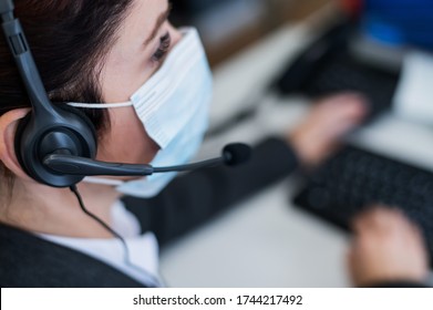 Close-up of a woman in a medical mask talking on a headset in an office. Portrait of a female call center operator during a virus outbreak. Business worker answer customer calls during outbreak covid.