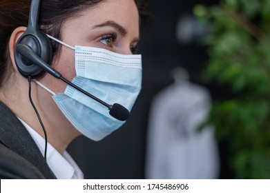 Close-up of a woman in a medical mask talking on a headset in an office. Portrait of a female call center operator during a virus outbreak. Business worker answer customer calls during outbreak covid.