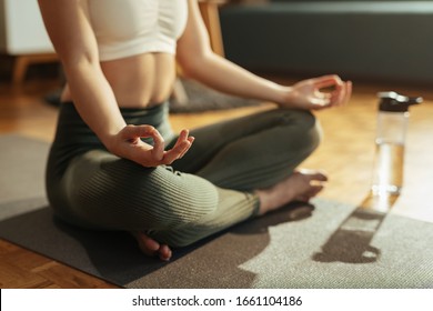 Close-up of woman meditating on lotus position at home. 