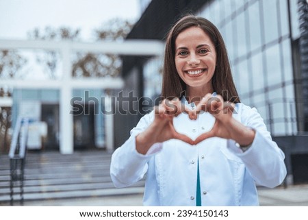 Closeup woman nurse making a heart shape with her hands while smiling and standing in hospital. Take care of your heart and love your body. Health and safety in the field of medicine 