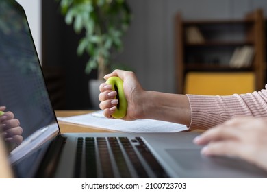 Closeup Of Woman Office Worker Gripping Rubber Expander In Hand While Typing On Laptop. Female Doing Exercises For Wrist Diseases Prevention While Working On Computer. Tunnel Syndrome Injury Concept