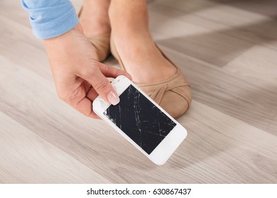 Close-up Of A Woman Picking Up The Broken Smart Phone From Hardwood Floor