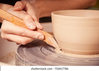 Close-up Woman potter beautifully sculpts from brown clay and equals a spatula with a deep plate on a potter's wheel in a beautiful workshop