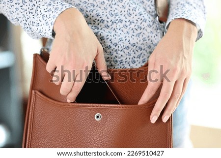 Close-up of woman putting smartphone in brown leather crossbody. Female take out cellphone of stylish bag