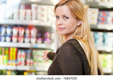 Close-up of woman reaching for products arranged in refrigerator and looking at camera - Powered by Shutterstock