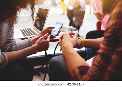 Closeup Of Woman Is Reading Text Message On Mobile Phone In Network, While Is Sitting With Laptop Computer In Co-working Cafe. Group Of Friends Are Using Gadgets During Recreation Time In Coffee Shop 