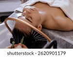 Close-up of a woman receiving a relaxing Japanese head spa treatment, with green massage sticks applied to her scalp, while water gently flows from a special tool during the session in a beauty salon