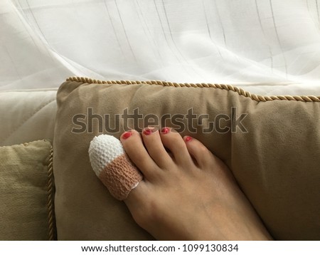 Closeup of woman right foot with a wounded big toe healed with band aid for medical care. Surgery is the result of a bad spa pedicure. Rest of the red toe nails are pretty.