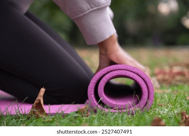 Close-up of woman rolling up yoga mat on grass in park - Powered by Shutterstock