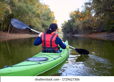 Closeup woman rowing in a green kayak in early autumn along the trees at the bank of Danube river - Powered by Shutterstock