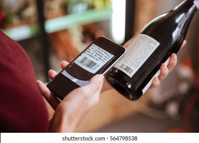 Closeup Of Woman Scanning Bar Code With Mobile Phone On Wine Bottle In Grocery Store