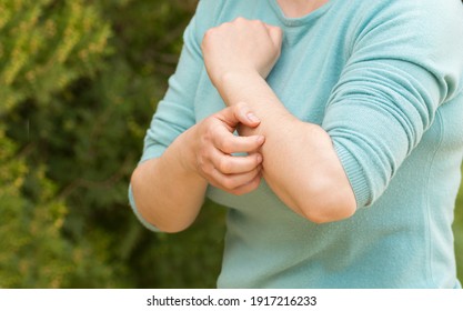 Close-up of woman scratching arm because it stings in a park with a green background - Powered by Shutterstock