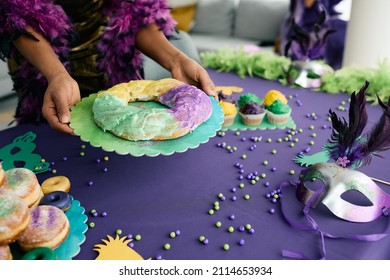 Close-up of woman serving King cake at dining table during Mardi Gras celebration party at home.