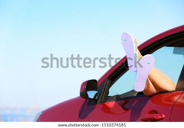 Closeup of woman showing legs with flip\
flops from car, space for text. Beach\
accessories