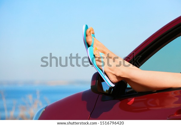 Closeup of woman showing legs\
with flip flops from car near sea, space for text. Beach\
accessories