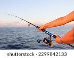 Close-up of woman sitting holding fish rod in hands. Female taking fish in sea or river. Fish and fishery concept