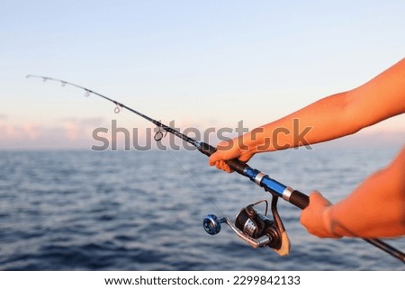 Close-up of woman sitting holding fish rod in hands. Female taking fish in sea or river. Fish and fishery concept