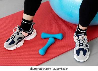 Close-up Of A Woman Sitting On A Blue Sports Ball, With His Feet On A Red Yoga Mat.