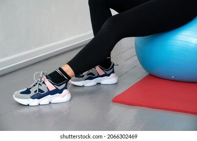 Close-up Of A Woman Sitting On A Blue Sports Ball, With His Feet On A Red Yoga Mat.