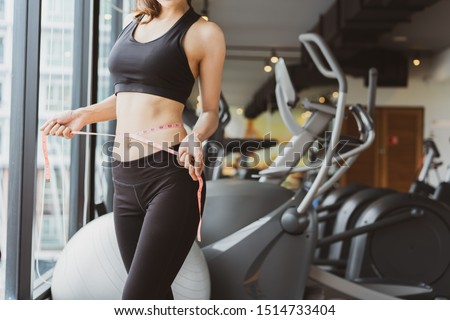 Closeup woman slim athlete using body fat measurement and waist size with waist line after workout at fitness gym healthy lifestyle weightloss happy in goal.