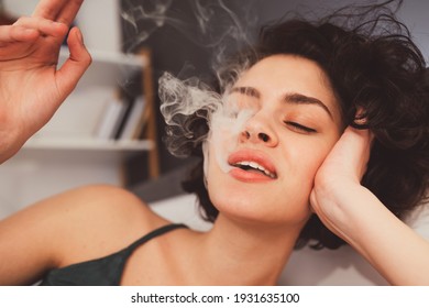 Close-up Of Woman Smoking Weed And Blowing Puffs Of Smoke While Having Funny Mood At Home. Stock Photo