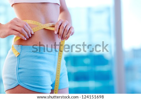 Close-up of a woman in sportswear measuring her waist