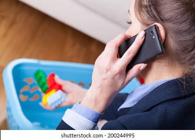 Close-up Of A Woman Talking On Phone And Cleaning Up Kids Toys