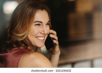 Closeup Of A Woman Talking Over Mobile Phone Looking Away. Portrait Of A Smiling Woman Holding A Phone To Her Ear.