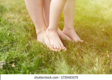 Closeup of woman and toddler kid barefeet on green grass outdoors. Happy young mother and toddler kid walking on the grass barefeet