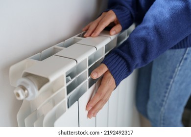 Closeup of woman warming her hands on the heater at home during cold winter days, top view. Female getting warm up her arms over radiator. Concept of heating season, cold weather. 