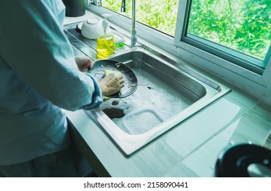 Close-up Of A Woman Washing Dishes With Dirty Food Scraps Cleaner In The Sink The Kitchen Counter At Home.