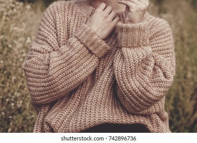 Closeup of woman wearing a beige soft oversized knitted sweater or jumper outdoors in the nature. Autumn fall scenery