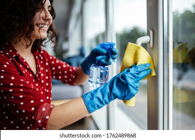 Closeup of woman wearing blue rubber gloves cleaning the window handle with microfiber rag and sanitizing spray during coronavirus pandemic quarantine. Health care and adaptation concept.
