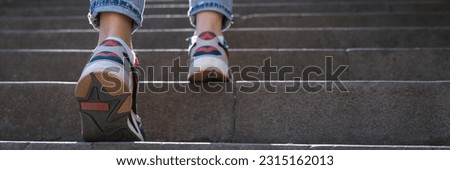 Close-up of woman wearing jeans and sneakers going up steep stairs. Female tourist in casual clothes walking upstairs outdoors