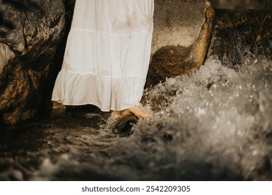 Close-up of a woman in a white dress standing with bare feet in a flowing stream near rocks, evoking calm and tranquility. - Powered by Shutterstock